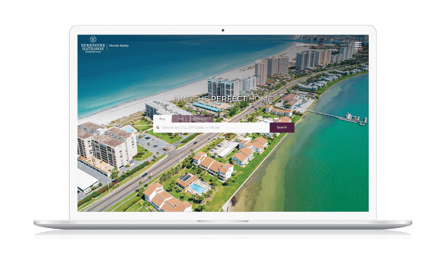 A laptop displaying the BHHS Florida Realty homepage, showing condos for sale on a beautiful barrier island in Florida.